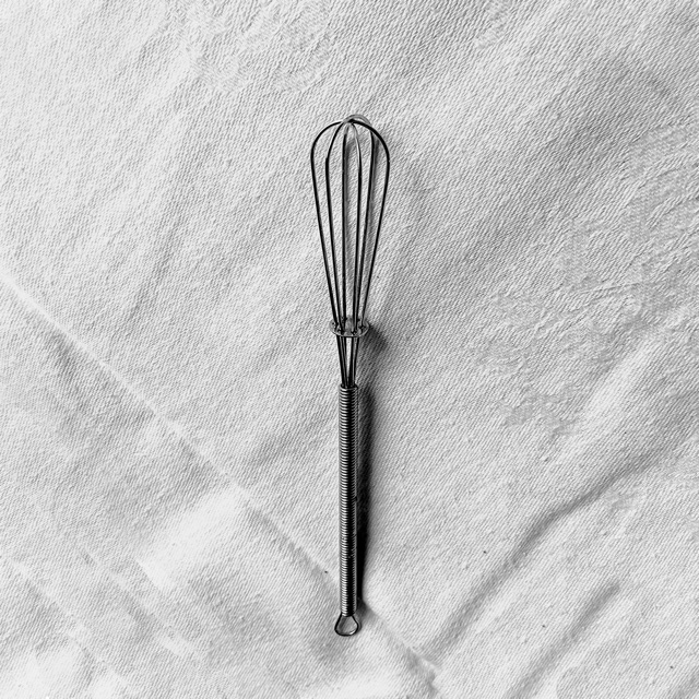 Black and white: a small wire whisk on a creased white cloth.