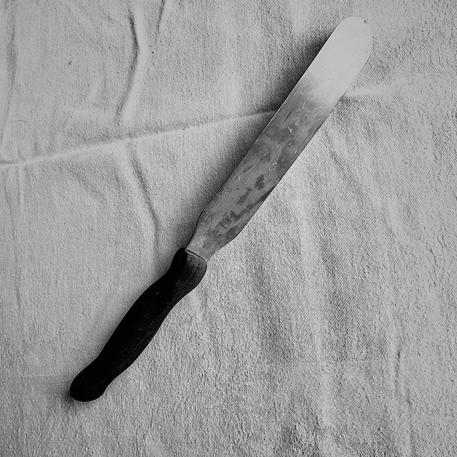 Black and white: a palette knife with a dark handle on a creased white cloth.