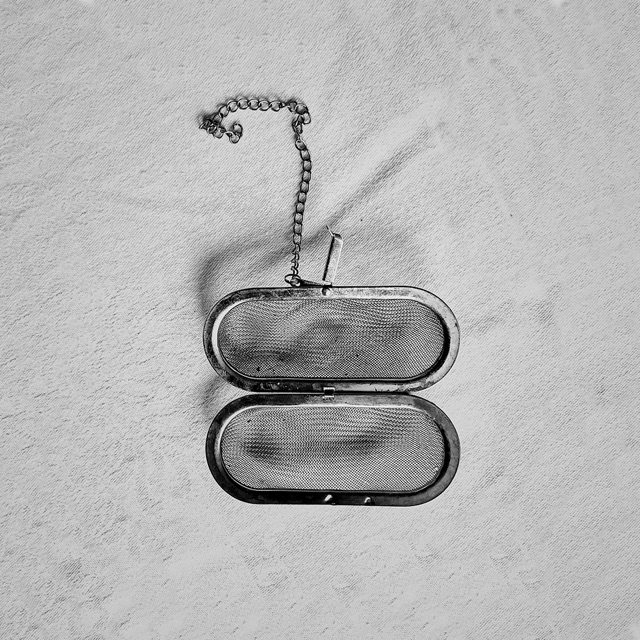 Black and white: an open mesh tea infuser on a chain, on a creased white cloth.