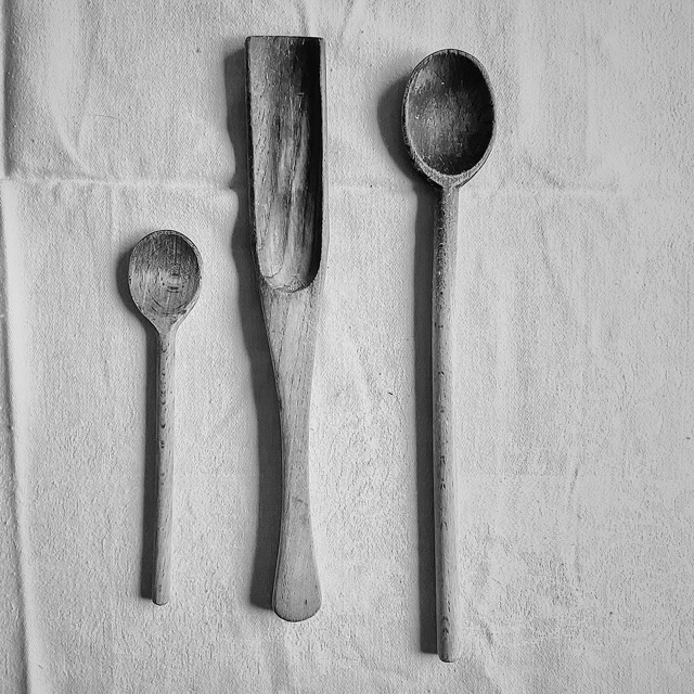 Black and white: two worn wooden spoons and a flat wooden scoop on a creased white cloth.