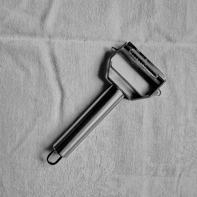 Black and white: a steel julienne peeler on a creased white cloth.