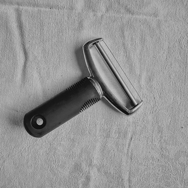 Black and white: a vegetable peeler with a dark ridged handle on a creased white cloth.